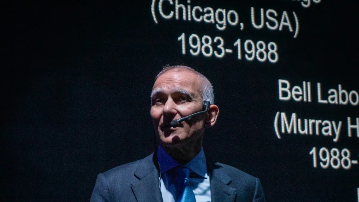A presenter with a headset microphone speaking in front of a projected slide